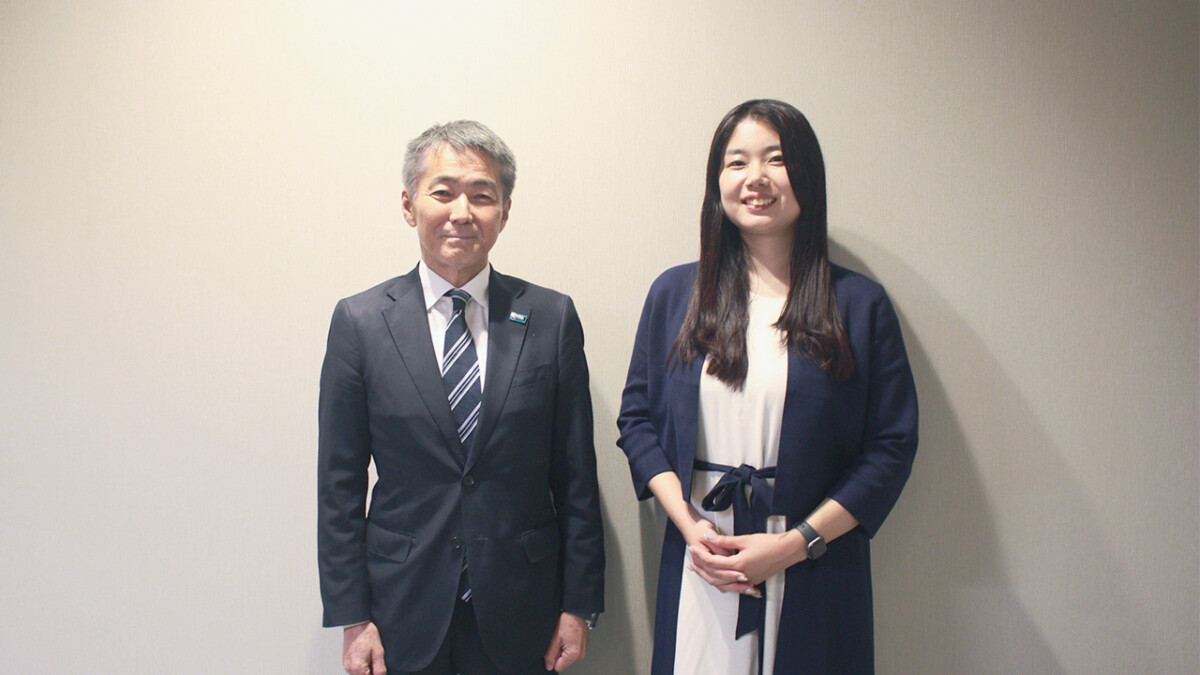 Two professionals posing for a photo: a gray-haired man in a suit and a young woman in a navy blazer, smiling against a plain wall.