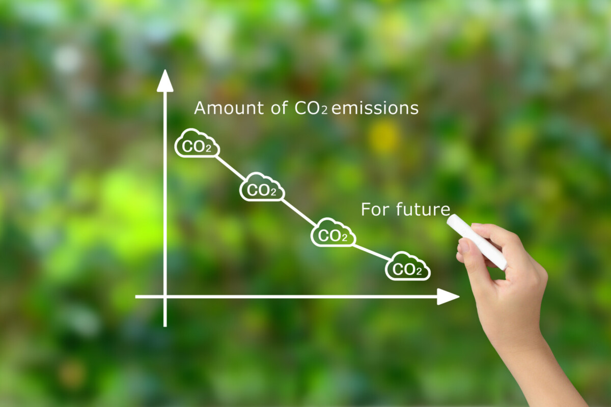 Hand drawing a descending CO2 emissions line on a white graph with cloud icons, using chalk on a green background.