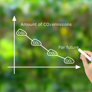 Hand drawing a descending CO2 emissions line on a white graph with cloud icons, using chalk on a green background.