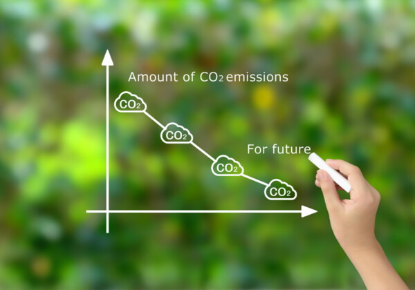 Hand drawing a descending CO2 emissions line on a white graph with cloud icons, using chalk on a green background.
