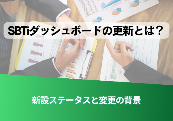 Japanese title text over a desk with charts reading 'SBTダッシュボードの更新とは？' and a green banner at the bottom that says '新設ステータスと変更の背景'—a business meeting/work context reviewing dashboards.