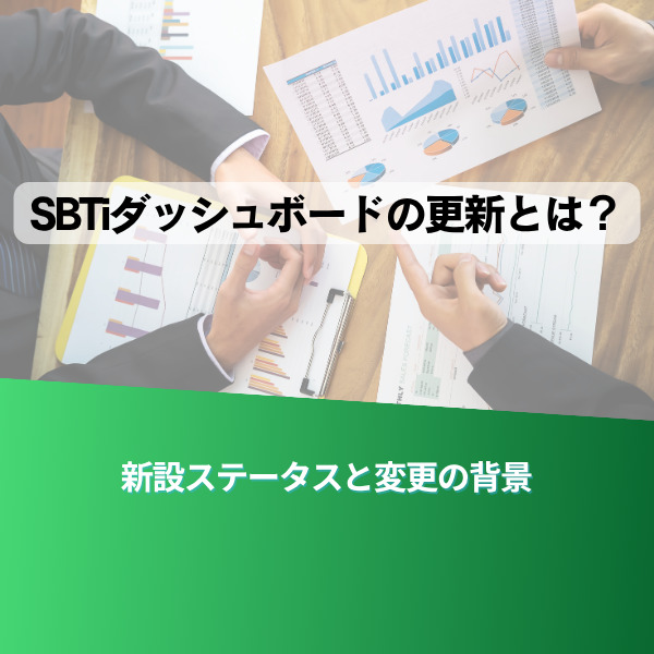 Japanese title text over a desk with charts reading 'SBTダッシュボードの更新とは？' and a green banner at the bottom that says '新設ステータスと変更の背景'—a business meeting/work context reviewing dashboards.